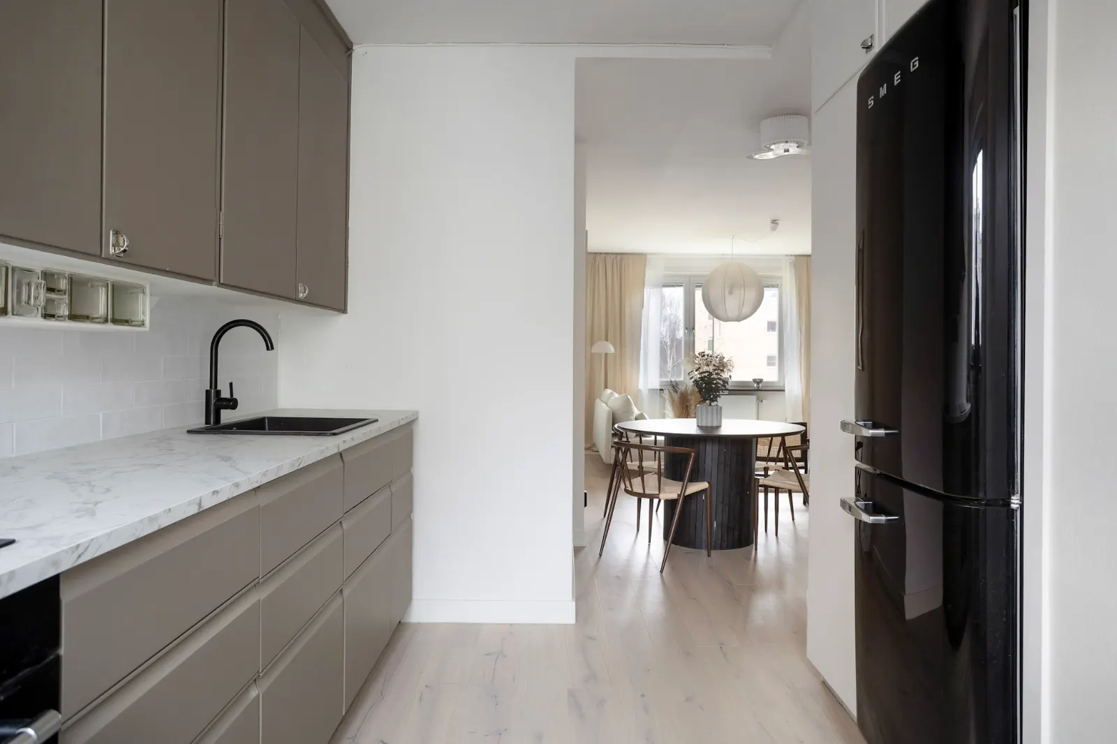 Ljust kök med vy mot matplatsen, fotograferat i bostadens verkliga skick utan AI-redigering